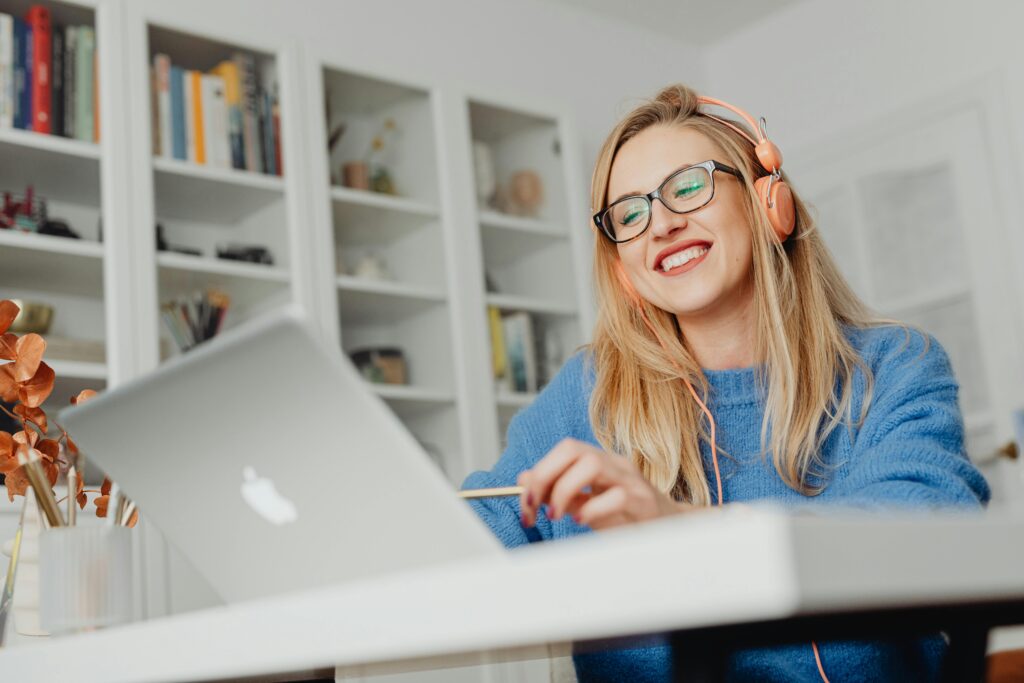 pexels-photo-5908493-5908493 Smiling woman wearing eyeglasses and headphones, working at home on a laptop.
